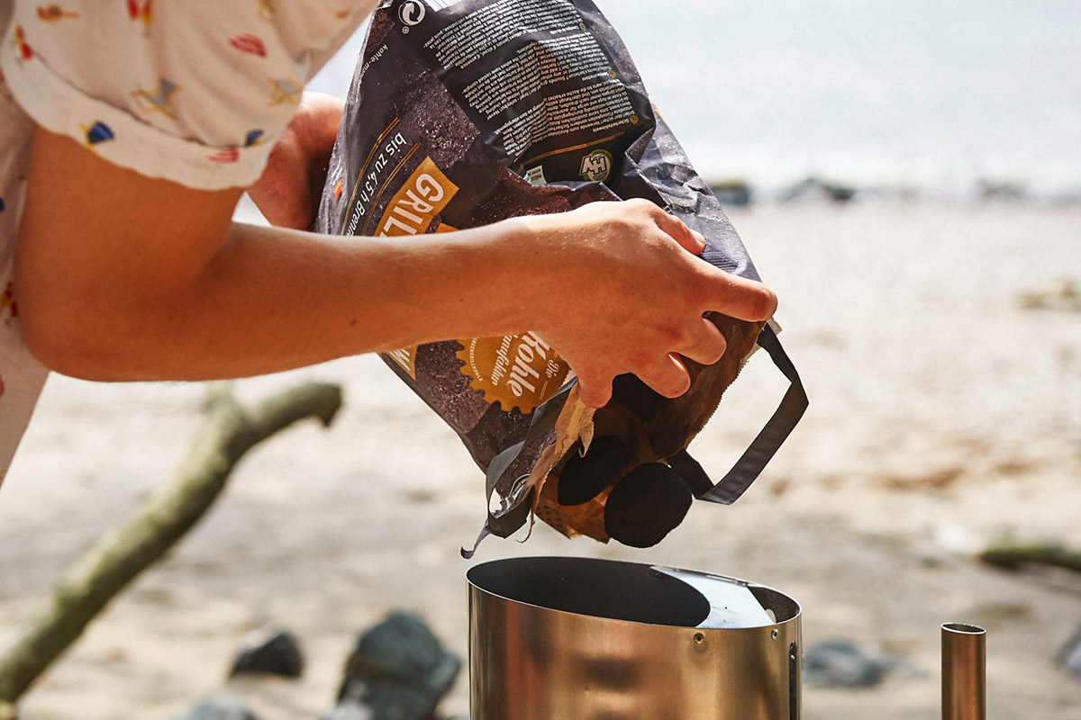 Man häller kol i Höfats BBQ Fire Starter på stranden