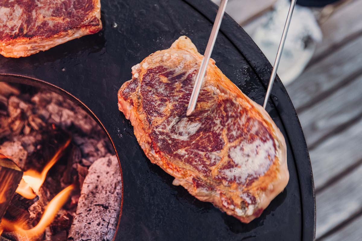 Grilltång lyfter på köttbit som grillas